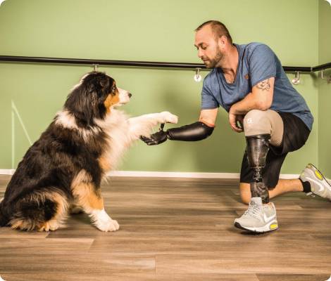Mann mit Arm- und Beinprothese und Hund, der Pfötchen gibt.