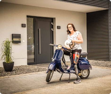 Frau auf Roller vor Haus mit Beinprothese